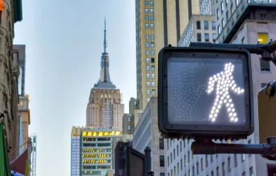 Close-up on pedestrian traffic signal with walk symbol lit up and Empire State Building spire visible in background.