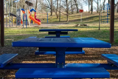Blue picnic table with attached benches and colorful children's playground in background.