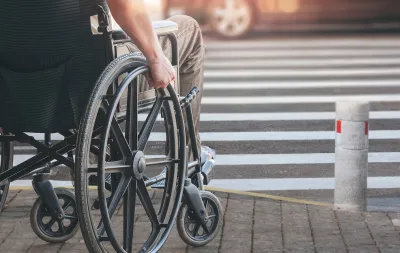Close-up of man in manually operated wheelchair waiting at urban crosswalk.