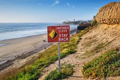 Red "Unstable Cliffs - Stay Back" sign on tall Pacific coast cliff