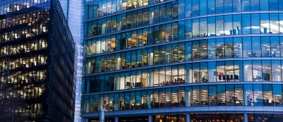 Close-up of glass facade of office building with office furniture visible through the windows.