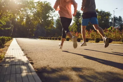 Two people run down a paved path in the city, surrounded by landscaping.