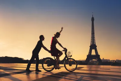 Silhouette of man holding on to back of bicycle ridden by woman with Eiffel Tower in background.