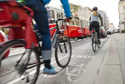 Cyclists in bike lane with red streetcar in background on urban street.