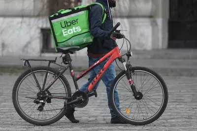 Person walking red bicycle with green Uber Eats delivery bag on cobblestone street in Bucharest, Romania.