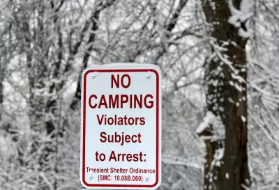White sign with No Camping - Violators Subject to Arrest and municipal code in red text with snowy trees in background.