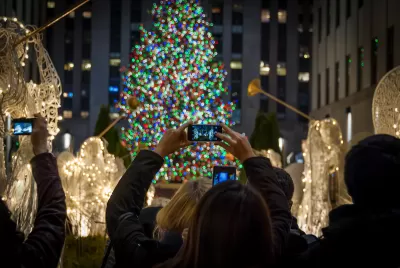 Tourists holding up cameraphones taking photos of Rockefeller Center Christmas tree in New York City.