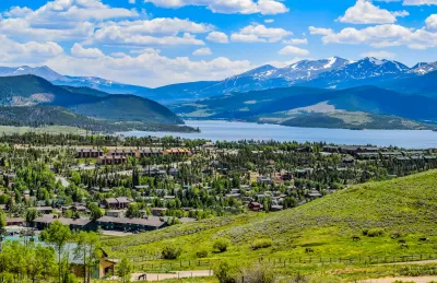 Scenic overlook of town with a lake and snowcapped mountains in the background.