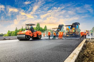 Crew in orange safety vests stand on roadway next to orange heavy equipment