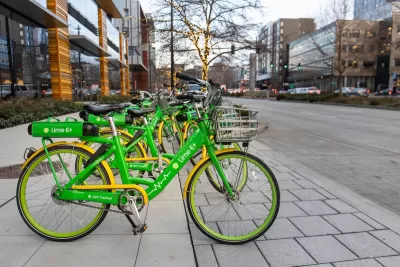 Row of green Lime electric bikes parked on sidewalk in Seattle with tree decorated with string lights in background.