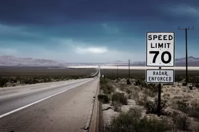 70 mph speed limit sign with bullet holes on southwestern highway with desert mountains in background.