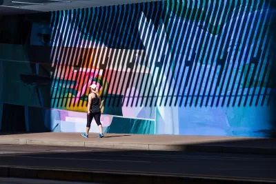Woman in exercise clothes walking on sidewalk against large wall with mural in Phoenix, Arizona.