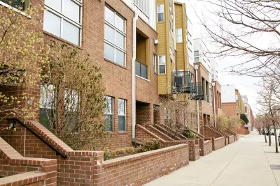 Row of light red brick condominium buildings along quiet street with concrete sidewalk in Denver, Colorado.