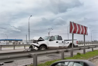 White truck with crumpled front sitting on highway after crash.