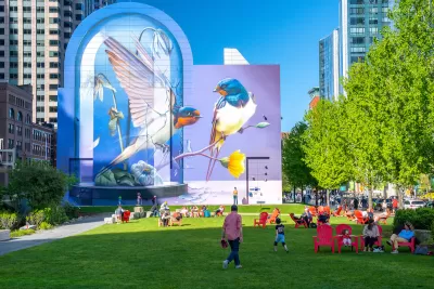 People enjoying a sunny day on a green lawn with pink lawn chairs and colorful bird mural in background in Boston, Massachusetts.