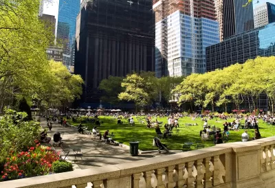 Green lawn in city park full of people sitting on lawn chairs with urban high-rises in background.