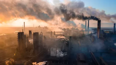 Aerial view of industrial plant with large smokestacks, surrounded by smoke with sunset sky in background.