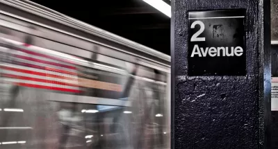 Close-up of 2 Avenue sign on column in NYC subway station with train passing by in background.