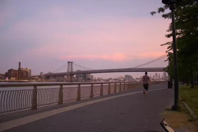 Sunset view of Williamsburg Bridge from East River Park walkway next to river with one jogger.