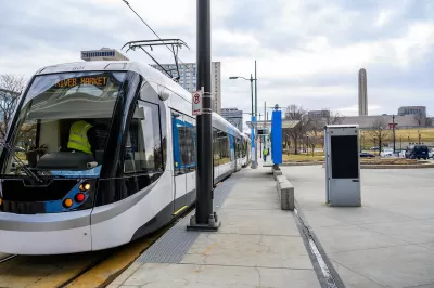 White and blue Kansas City streetcar at a station with LIberty Memorial column in background.