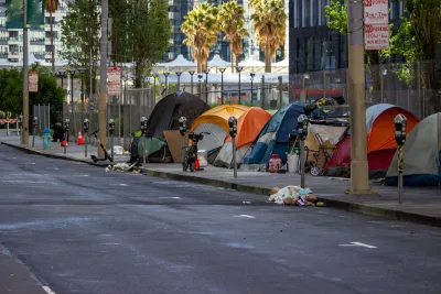 Line of tents set up against a fence on a public sidewalk in San Francisco, California with bikes and personal items around.