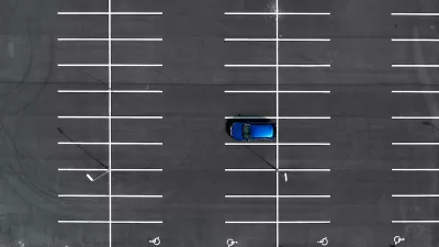 Bird's eye view of empty asphalt parking lot with one blue car.