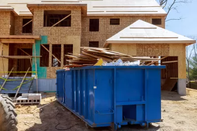 Large blue metal dumpster container in front of wood-frame house under construction.
