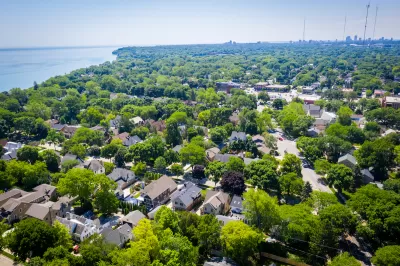 Aerial view of large homes surrounded by mature trees with Lake MIchigan shoreline at left.