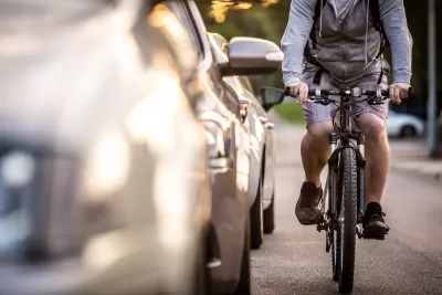 Man on bike rides next to parked cars.