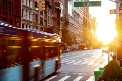 Blurred image of New York City bus driving through intersection with 5th Avenue with golden hour sunset sky in background.