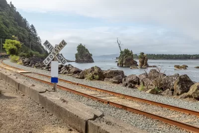 Railroad crossing sign next to tracks along rocky coast in Oregon.