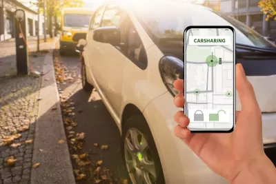 Close-up of hand holding up phone with car sharing app open in front of parked cars.