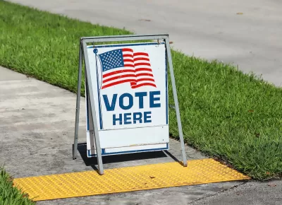 "Vote Here" sandwich board sign with American flag on sidewalk in Fort Lauderdale, Florida.