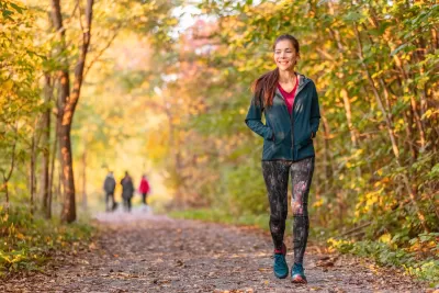 Woman in leggings and long-sleeved jacket walks in public park among fall foliage