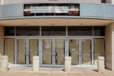 Vacant retail storefront with multiple glass doors lined with brown paper and a removed neon sign.