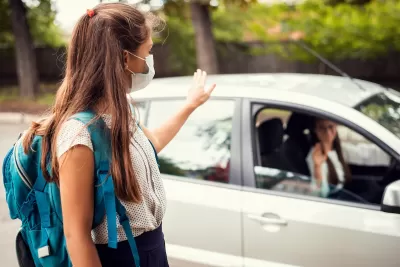 Girl wearing Covid mask and backpack getting dropped off by mom at school.