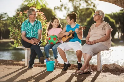 Grandparents sitting on bench with young girl and boy, girl holding ball and boy holding ukelele.