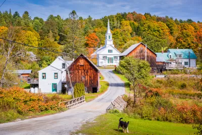 Rural community qith quaint homes and white steepled church against forest with fall colors and German shepherd dog in foreground.