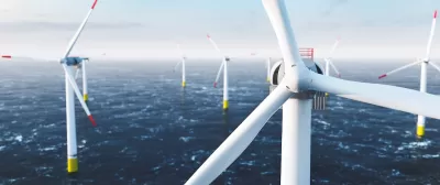 Close-up of top of white offshore wind turbine with other turbines in sea in background.