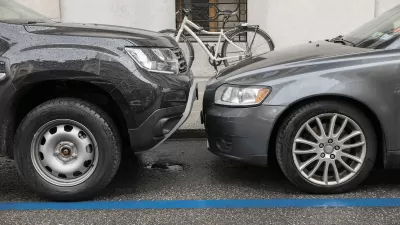 Two grey cars parked nose to nose, one taller than the other, on city curb with parked bicycle visible on sidewalk.