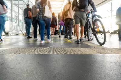 Walkways and escalator at crowded transit station, with one person walking a bike in foreground.