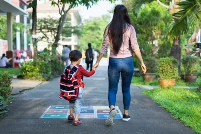 View from back of mother and hcild holding hands and walking down asphalt walkway painted with game grid.