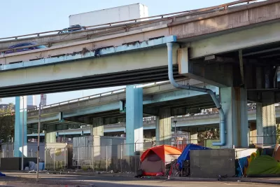 Tents set up against fence by unhoused people under freeway overpass in San Francisco, California.