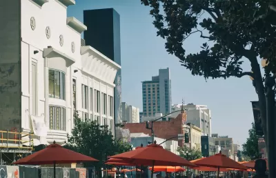 The tops of umbrellas for outdoor dining spaces are visible with large buildings in the background on a sunny day in the city of San Diego.