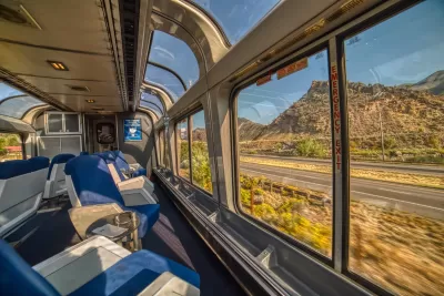 View from inside glass top floor of Amtrak passenger train with Rocky Mountains scenery outside.