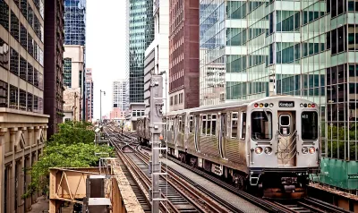 Silver Chicago train passing by dense high-rise buildings on elevated track.