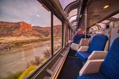 Amtrak train with large curved windows passing through scenic Rocky Mountain red rock canyon