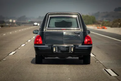 Black hearse seen from behind driving on multilane road.