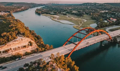 Aerial view of Pennybacker Bridge in Austin, Texas. Bridge over river with orange arches and downtown Austin visible in far background.