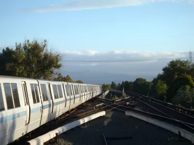 BART heavy rail train on elevated track pulling into Concord, CA station with cloudy sky and trees in background.